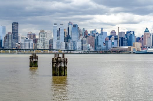 View of Manhattan Skyline with Hudson river and wooden boat docks in front, New York City during cloudy winter day, horizontal