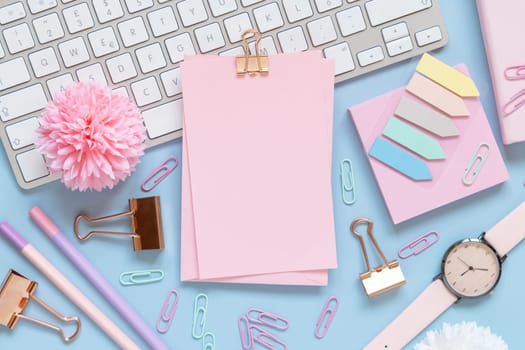 Paper with a clip, Pink school accessories and keyboard on light blue , Top view, mockup. Girly workplace with notebook, scissors, pencil, pen, paperclips, cards and watch. Back to school