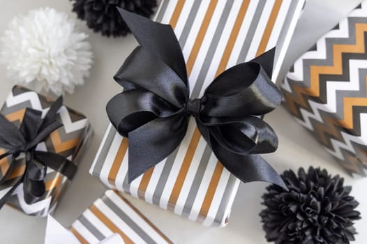 Gift boxes wrapped in Striped and chevron geometric paper with black ribbon bows near black and white decor close up. Christmas, New Year, Birthday, Anniversary concept