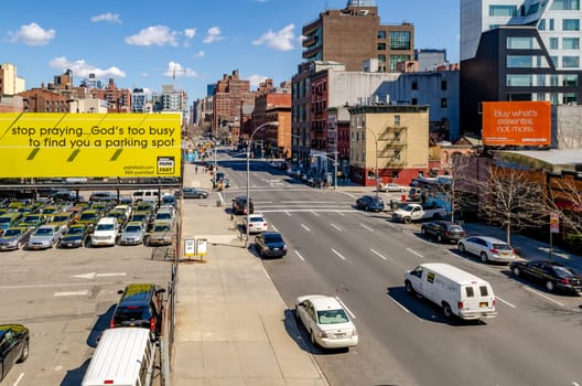 City street in Chelsea with advertisement posters, traffic and lots of parked cars, aerial view from the High Line Rooftop Park, New York City during sunny winter day, horizontal