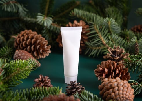 Natural organic cosmetic cream in white plastic tube near fir branches and pine cones on dark green close up. Brand packaging mockup for skincare product. Healthcare cosmetics concept