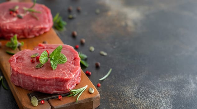 Raw beef fillet steaks on wooden board on dark background close up. Portioned filet mignons with spices and herbs. Concept of summer food