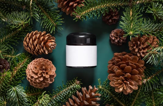 Brown glass jar near fir branches and pine cones on dark green top view. Brand packaging mockup. Skincare beauty product, cream or serum. Healthcare natural cosmetics concept
