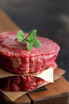 Raw beef fillet steaks on wooden board on dark background close up. Portioned filet mignons with spices and ingredients. Concept of summer food