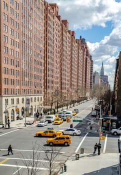 Crossroads at Chelsea, New York City with lots of yellow taxi cabs and cars passing by during sunny winter day, Brown Building facades in the background, vertical