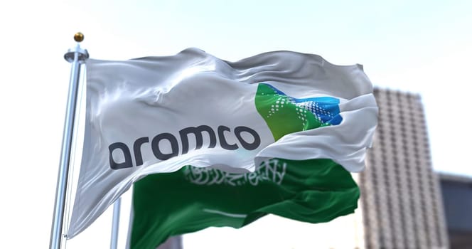 Dhahran, SA, March 2022: The flag of the Aramco oil company waving in the wind with the national flag of Saudi Arabia blurred in the background. Aramco is the Saudi national hydrocarbon company