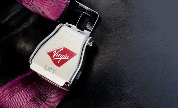 London, UK, July 2021: Purple belt of an empty seat inside an airplane with the Virgin Atlantic airlines logo printed on the metal. Virgin Atlantic is a British airline. Safety measure for air travel