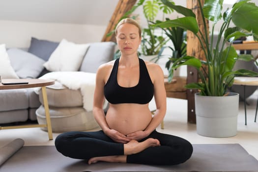 Young beautiful pregnant woman training yoga, caressing her belly. Young happy expectant relaxing, thinking about her baby and enjoying her future life. Motherhood, pregnancy, yoga concept