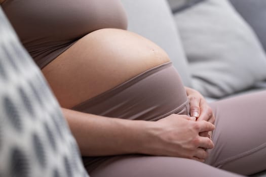Pregnant woman belly. Pregnancy Concept. Pregnant tummy close up. Detail of pregnant woman relaxing on comfortable sofa at home