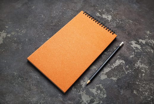 Photo of blank orange notepad and pencil on concrete background. Branding mock up. Space for text.