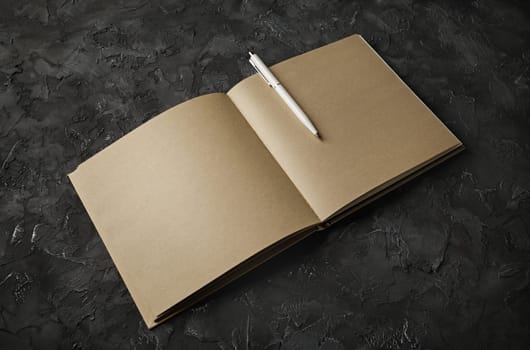 Blank kraft sketchbook and pen mock up on black plaster background.