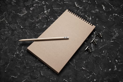 Blank kraft notebook and pencil on black plaster background. Mock-up for design presentations and portfolios.