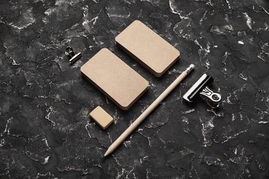 Blank kraft business cards, pencil, eraser and clip on black plaster background. Blank stationery set.