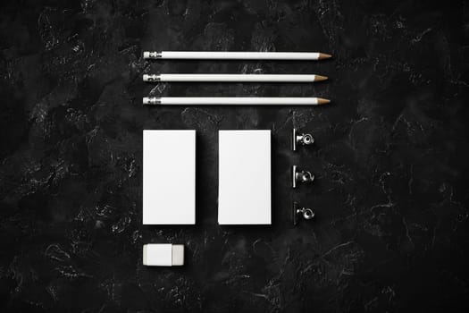 Blank business cards, pencils, eraser and clips on black plaster background. Template for graphic designers portfolios. Top view. Flat lay.