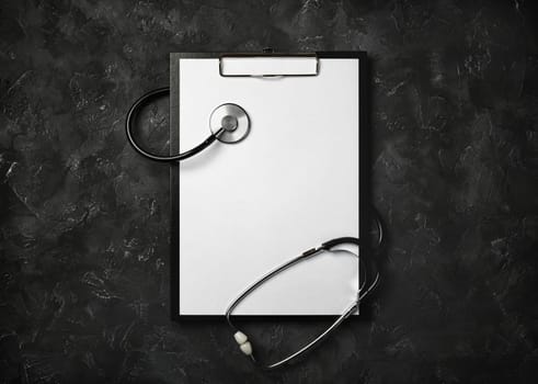 Blank medical clipboard with stethoscope on black plaster background. Copy space for text. Flat lay.