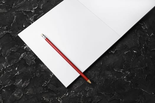 Blank open sketchbook and pencil on black plaster background. Responsive design template.