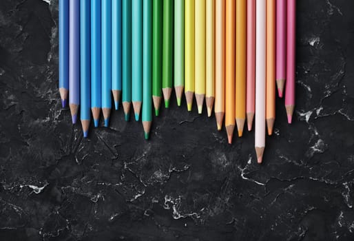 Beautiful color pencils for drawing on black plaster background. Top view. Flat lay.