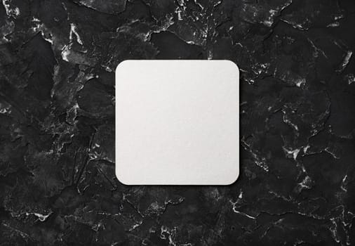 Blank square beer coaster on black plaster background. Flat lay.