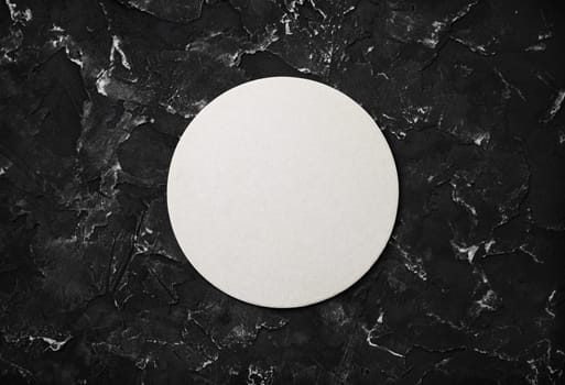 Photo of blank beer coaster on black plaster background. Flat lay.