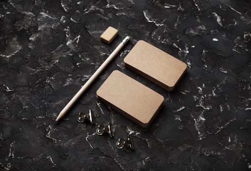 Photo of blank vintage business cards, pencil, eraser and clips on black plaster background. Branding mock up.