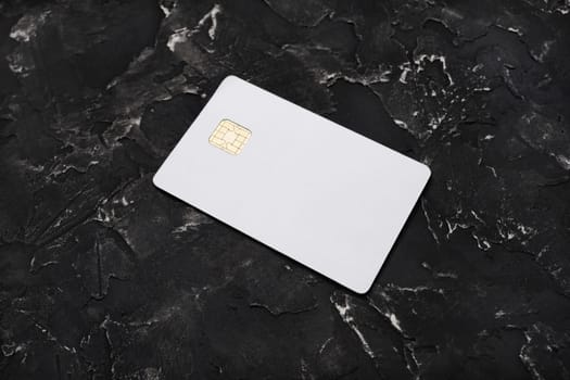 Blank credit card on black plaster background. Photo of white bank card. Mockup for branding identity.
