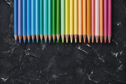 Row of colorful pencils on black plaster background. Top view with copy space. Flat lay.