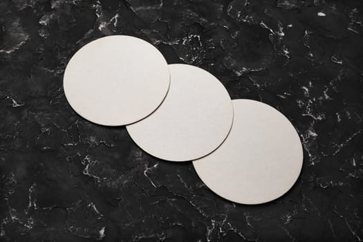 Photo of three blank beer coasters on black plaster background.