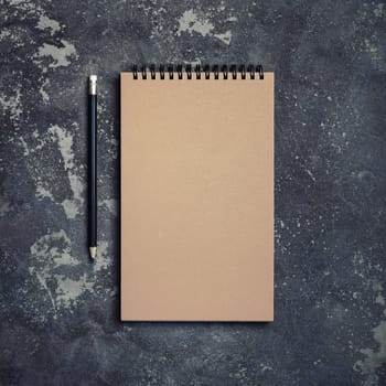 Photo of blank kraft notebook and pencil on concrete background. Top view. Flat lay.