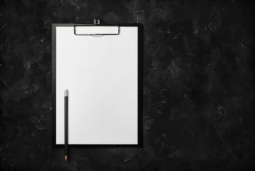 Blank clipboard and pencil on black plaster background. Copy space for text. Top view. Flat lay.