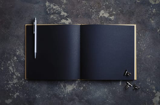 Blank black brochure, pen and clips on concrete background. Template for placing your design. Top view. Flat lay.