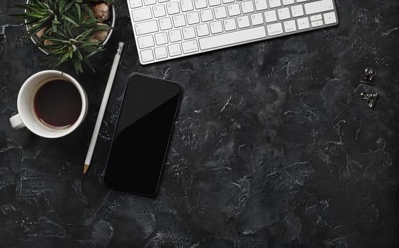 Top view of work space with keyboard, smartphone, coffee cup, succulent plant and pencil on black plaster background. Flat lay.