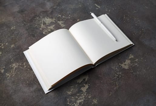 Photo of opened book with blank white pages and pen on concrete background.