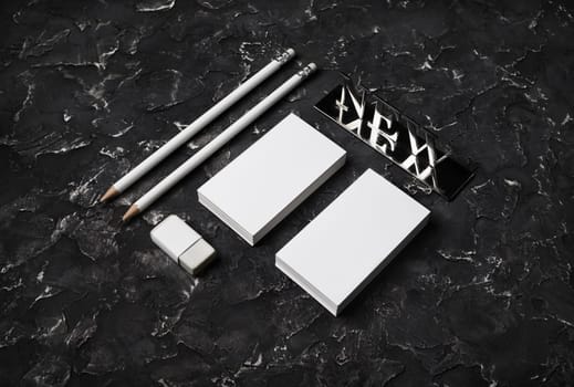 Blank stationery template. Blank business cards, pencils, eraser and new metal plate on black plaster background.