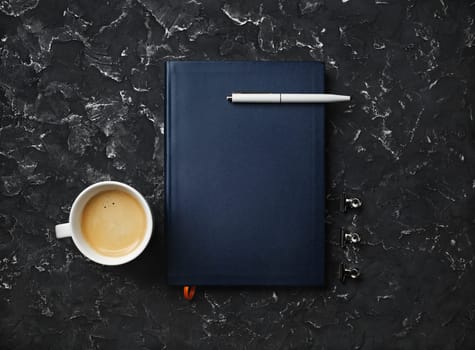 Blank notepad, pen, coffee cup and clips on black plaster background. Top view. Flat lay.