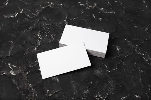 Blank business cards on black plaster background. Mockup for branding identity. Studio shot.
