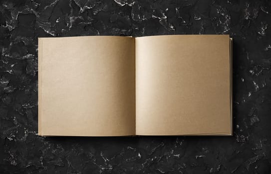 Blank kraft sketchbook, brochure or book on black plaster background. Responsive design mockup. Top view. Flat lay.