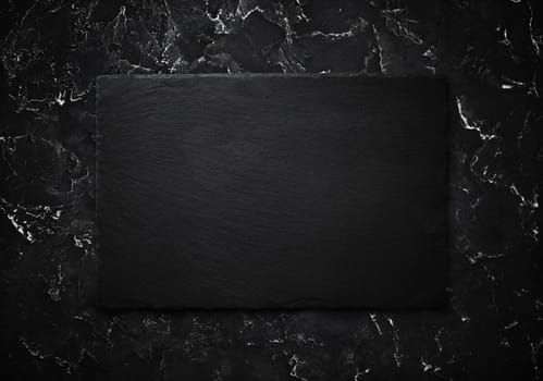 Photo of blank black stone slate plate on black plaster background. Top view with copy space. Flat lay.