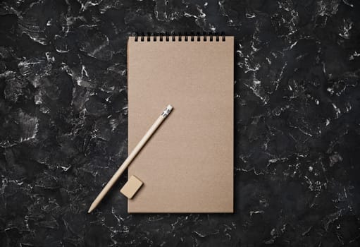 Blank kraft spiral notebook, pencil and eraser on black plaster background. Top view with copy space. Flat lay.