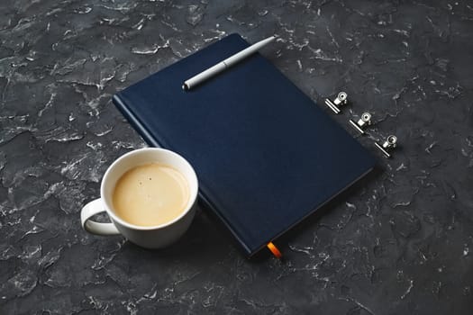 Blank closed book, pen and coffee cup on black plaster background. Responsive design template.