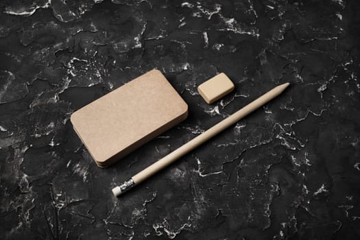 Photo of blank kraft business cards, pencil and eraser on black plaster background. Template for branding identity.