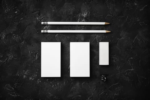 Blank business cards, pencils and eraser on black plaster background. Blank stationery template. Top view. Flat lay.