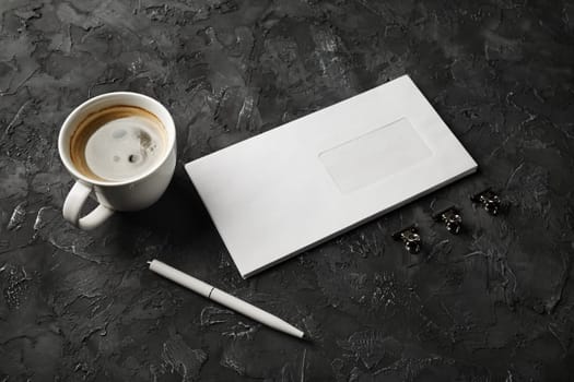 Blank envelope, coffee cup, pen and clips on black plaster background. Branding mock up.