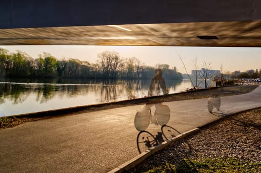 bike / biking person (translucent) on a riverside underneath a bridge , digitally processed