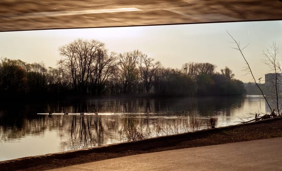 Cycle way underneath a bridge, next to a river in a sunny early daytime atmosphere with sun light reflections