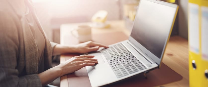 Woman with smartphone in her hand working on the laptop in office. Place of work. Close-up view.