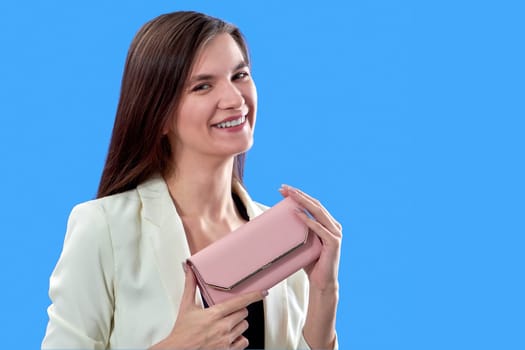 A beautiful young woman is holding a pink purse on a blue background, copy space. High quality photo