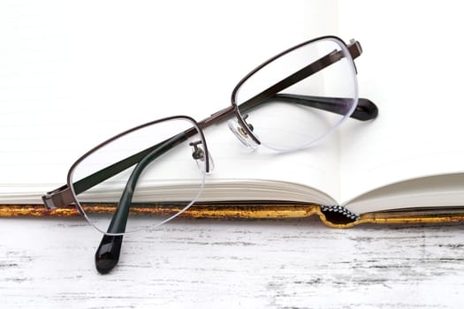 Stylish eyesight glasses and opened notebook on white wooden table
