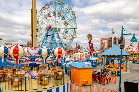 Luna Park Amusement Park at Coney island, Brooklyn, different rides and People waiting in Line during Jewish National Day, New York City, winter day with cloudy sky, Residential Building in the background, horizontal