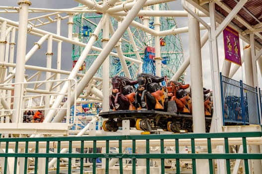 Steeplechase Coaster closed, empty at Luna Park Amusement Park, view of the train in the station, Coney island, Brooklyn, New York City during winter day with cloudy sky, Wonder Wheel in the Background, horizontal