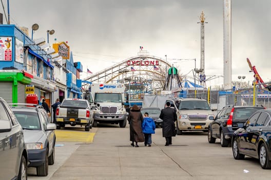 Jewish National Day at Luna Park Amusement Park, Coney island, Brooklyn, New York City during winter day with cloudy sky, Family walks in the direction of the Park, lots of cars parked next to the street, horizontal